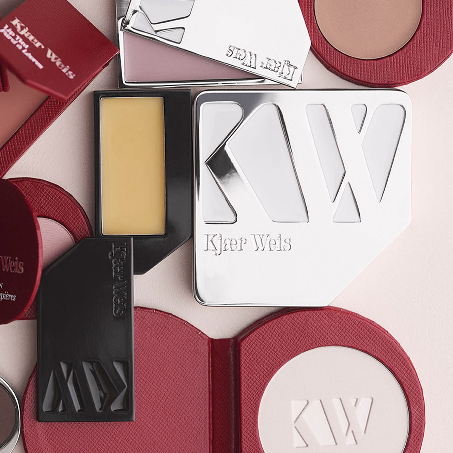 Kjaer Weis makeup products including a compact and a stick on a light pink background.